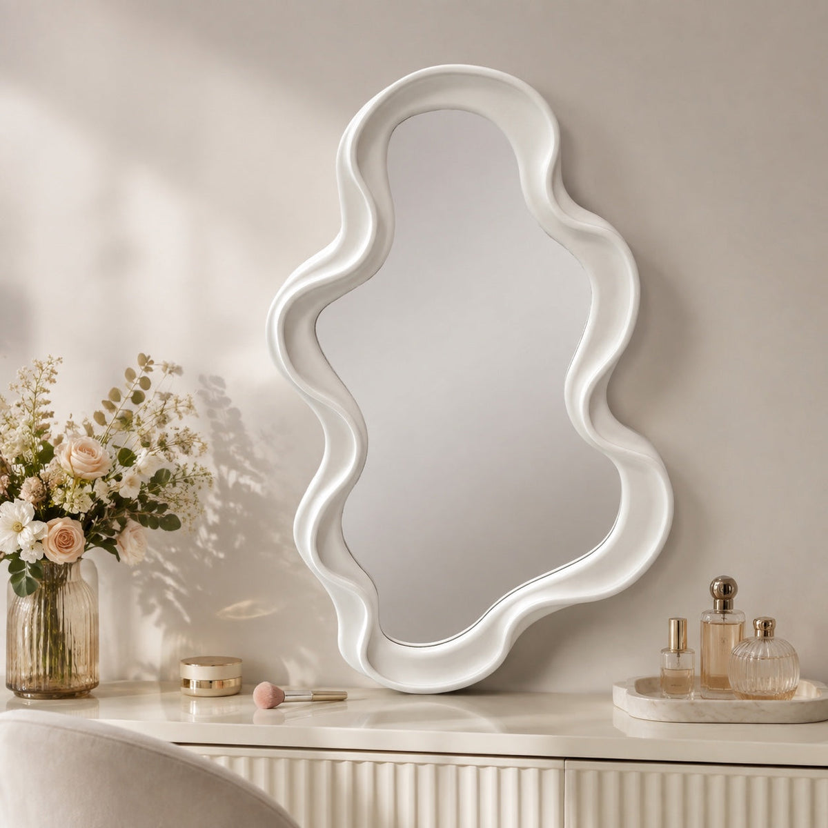 Cream sculptural wavy framed mirror styled on white vanity with flowers